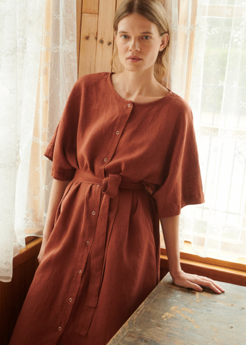 model leaning on the table posing in oversized linen dress in terracotta with snap openings