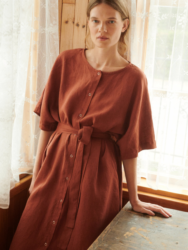 model leaning on the table posing in oversized linen dress in terracotta with snap openings