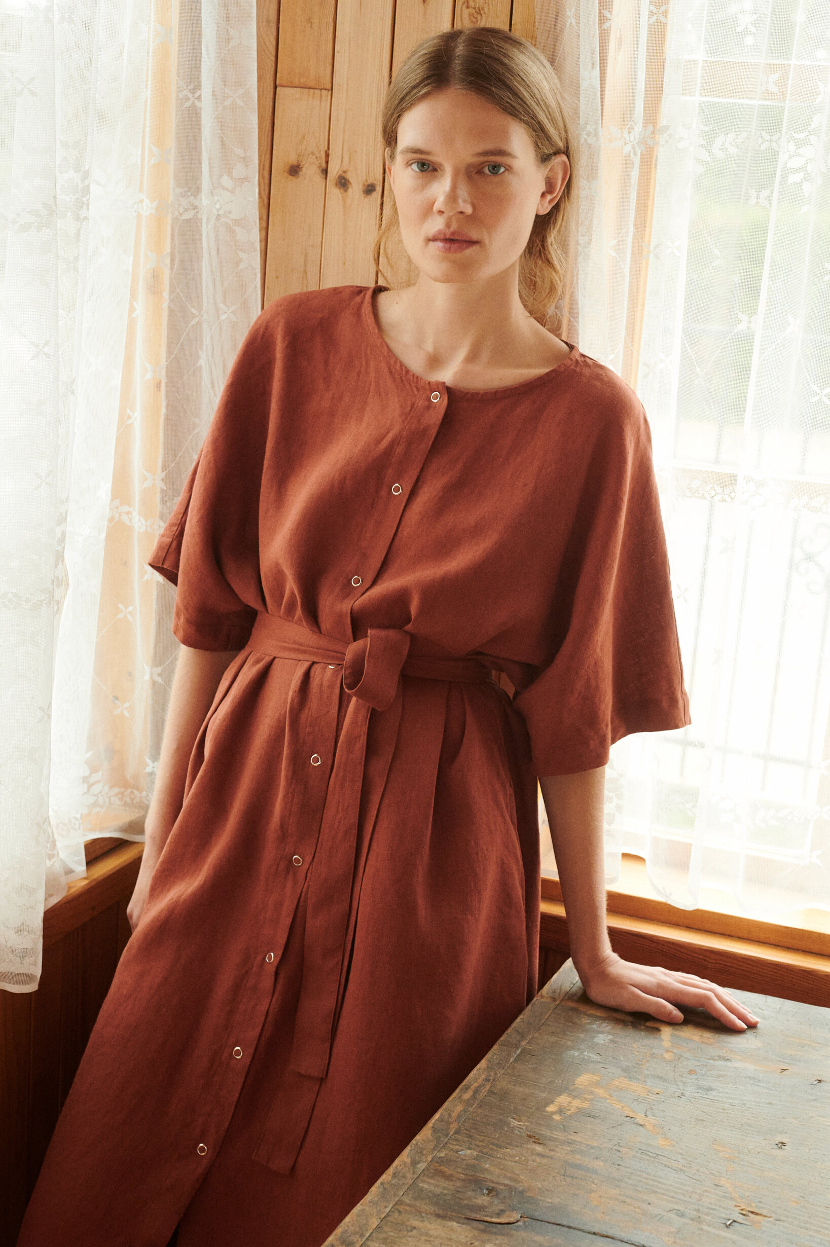 model leaning on the table posing in oversized linen dress in terracotta with snap openings
