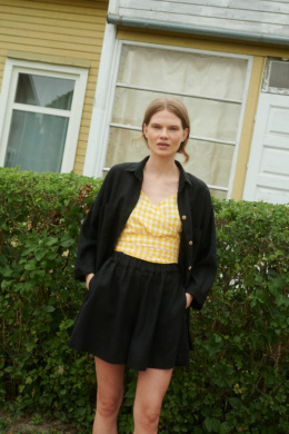 Model wearing black linen shorts, yellow gingham linen top and black linen shirt
