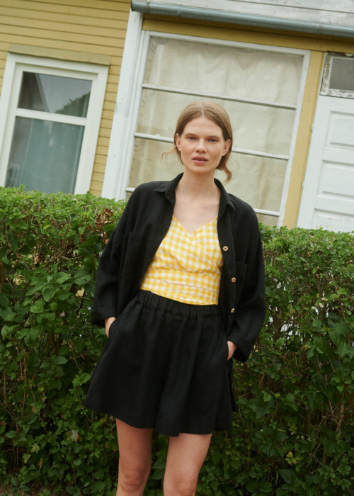 Model wearing black linen shorts, yellow gingham linen top and black linen shirt