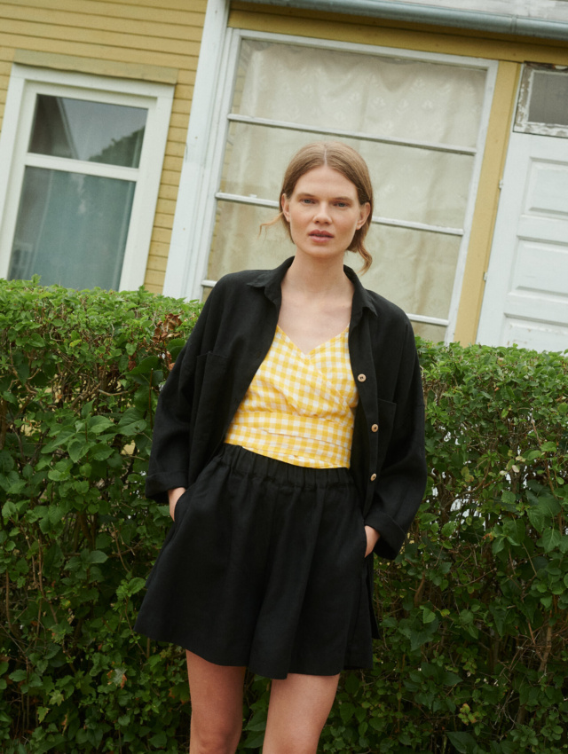 Model wearing black linen shorts, yellow gingham linen top and black linen shirt