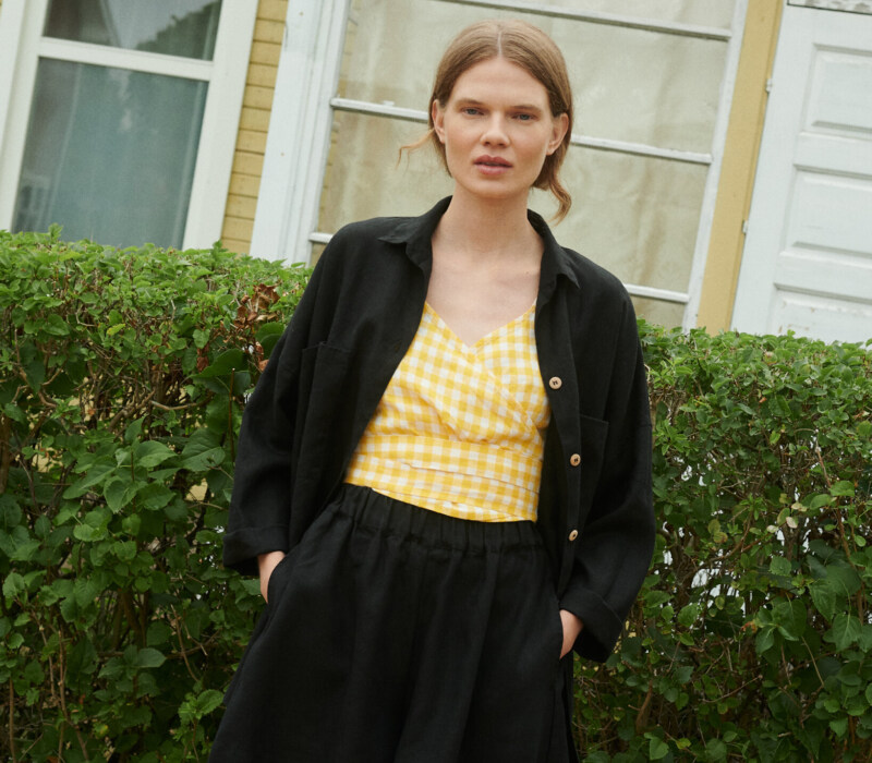 Model wearing black linen shorts, yellow gingham linen top and black linen shirt