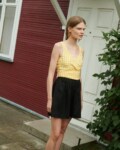 a girl wearing linen wrap top in yellow gingham and black linen shorts near the summer house