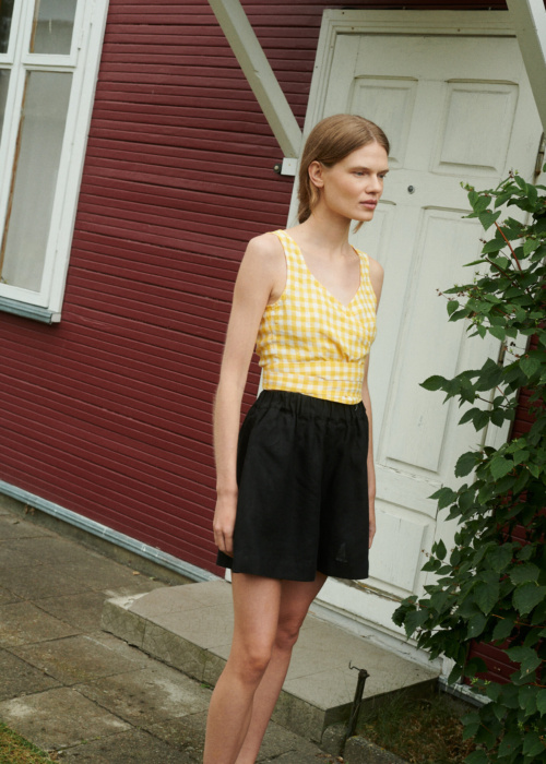 a girl wearing linen wrap top in yellow gingham and black linen shorts near the summer house