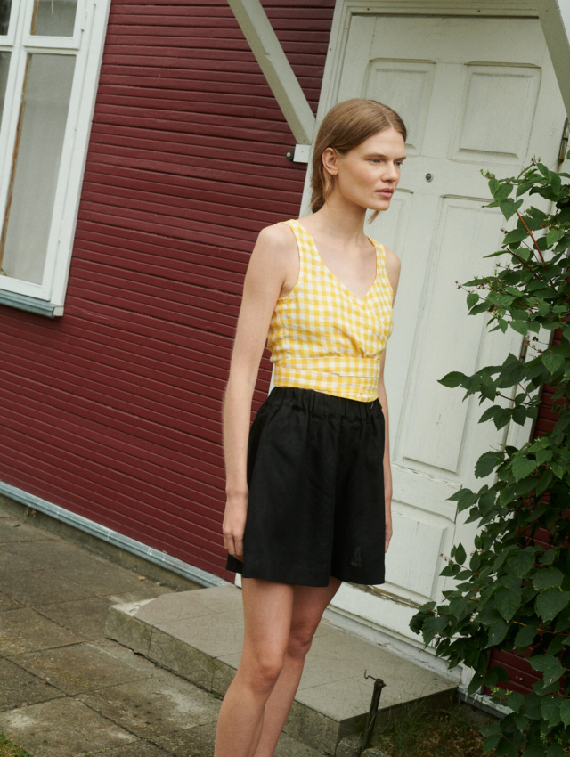 a girl wearing linen wrap top in yellow gingham and black linen shorts near the summer house