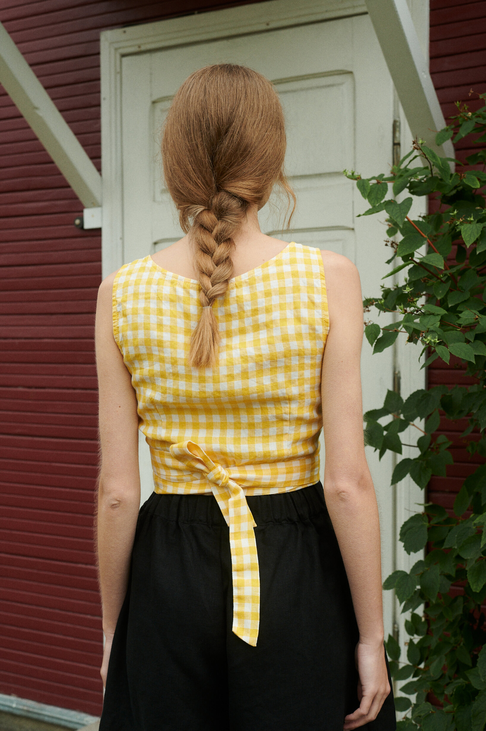 a back view of model wearing yellow gingham summer wrap top and vlack shorts