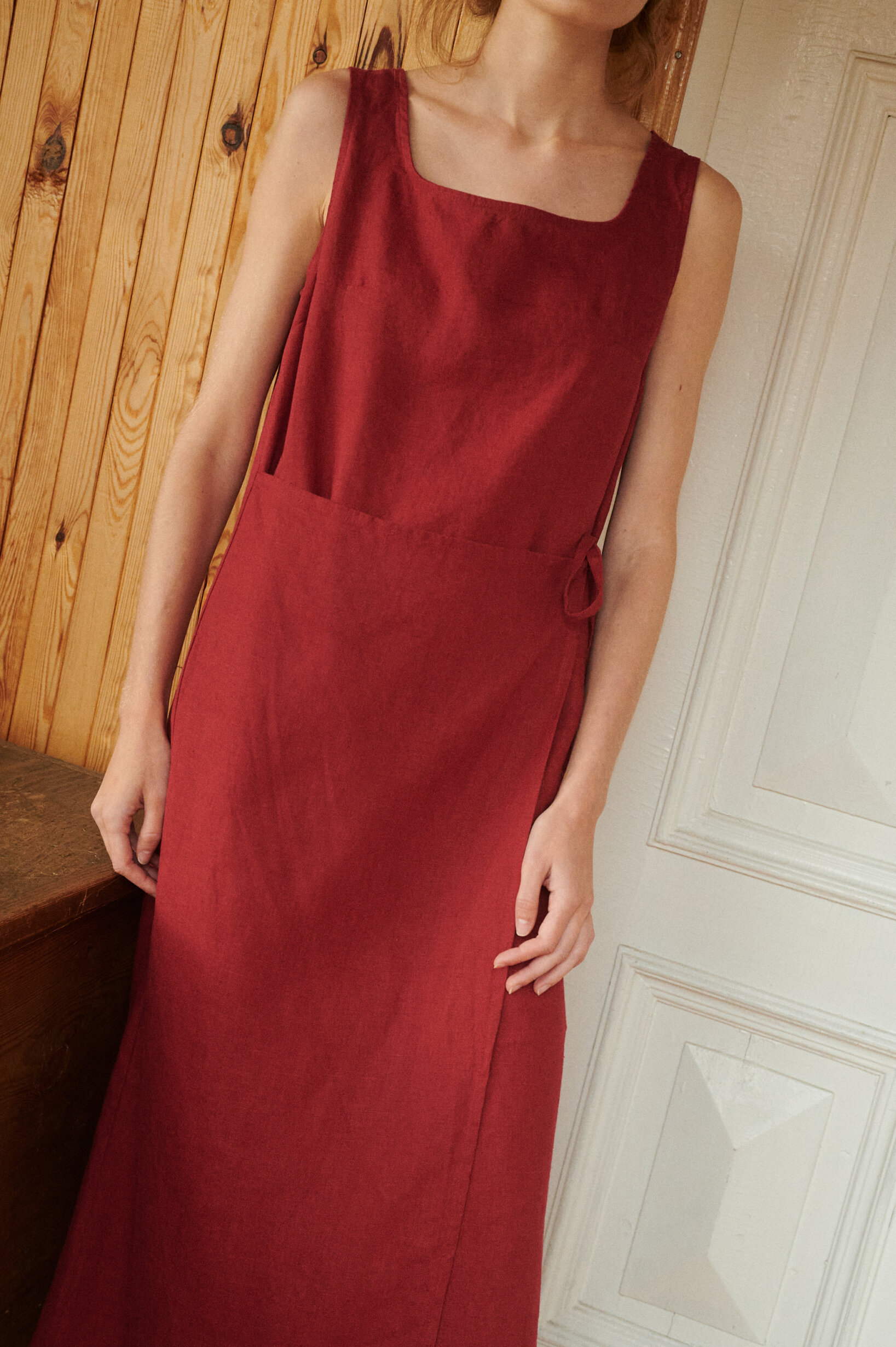 a close up of a woman wearing sleeveless summer wrap dress in burgundy red linen