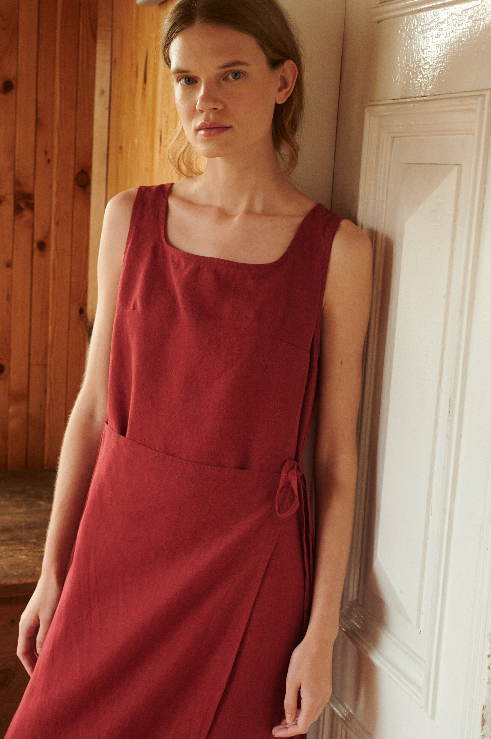 a close up shot of a model wearing sleeveless summer wrap dress in burgundy red linen