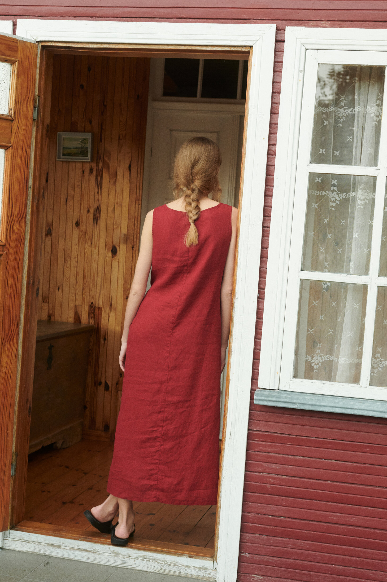 a back view of the sleeveless wrap dress in burgundy red linen in a summer cottage