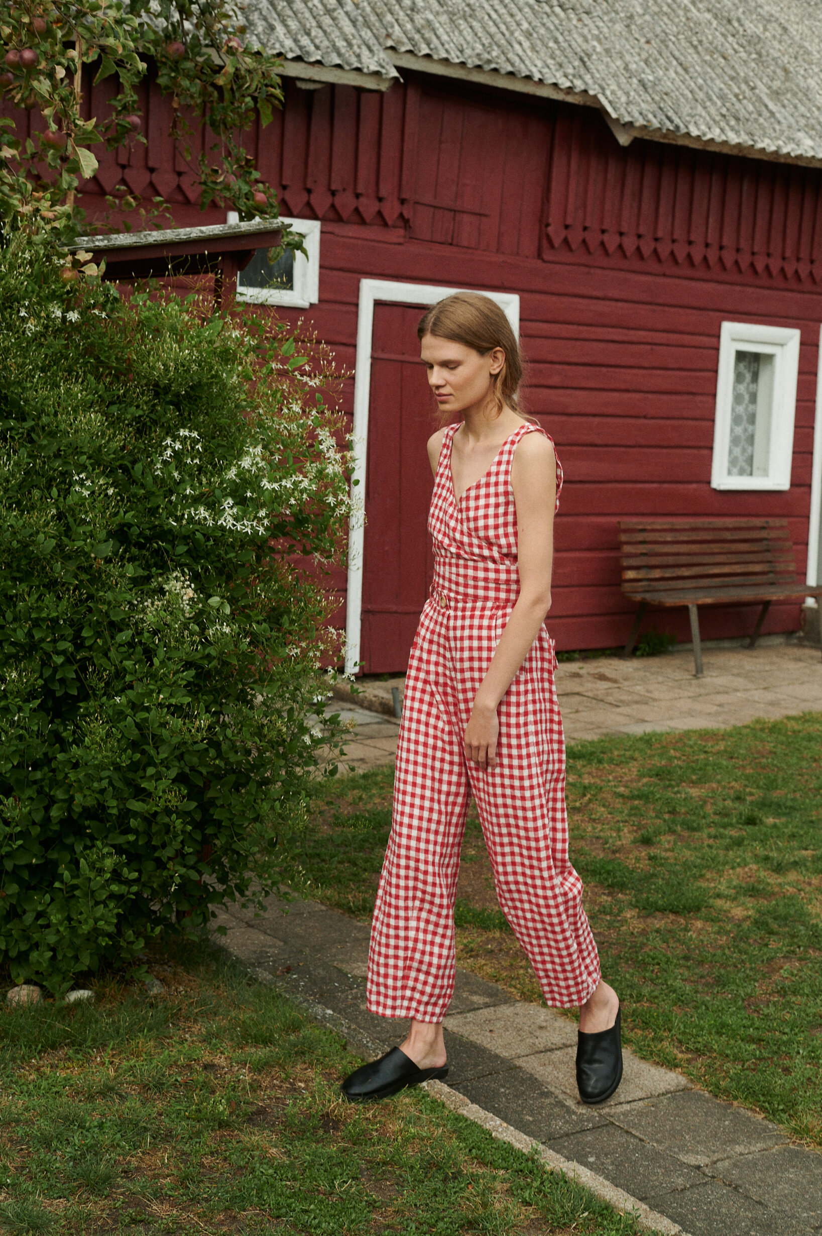 Model at he garden near the summer cottage wearing summer linen set of wrap top and barrel leg trousers in red gingham linen.