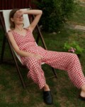Model sitting on a chair wearing summer linen set of V-neck wrap top and barrel leg trousers in red gingham linen.