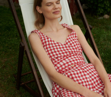 Model sitting outside in a garden wearing summer linen set of wrap top and trousers in red gingham linen.
