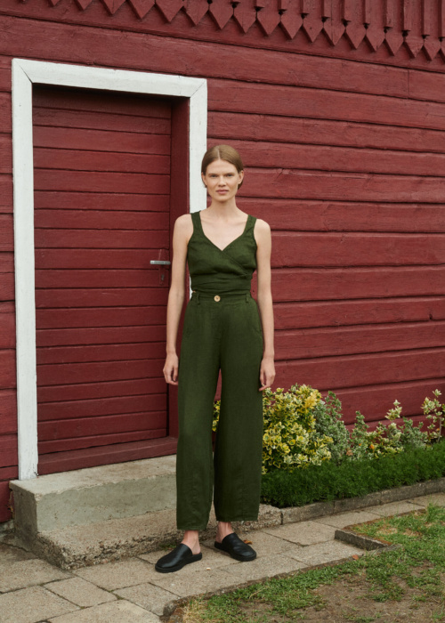 Model posing in summer clothing set of waffle linen trousers and wrap top in forest green near the red summer cottage