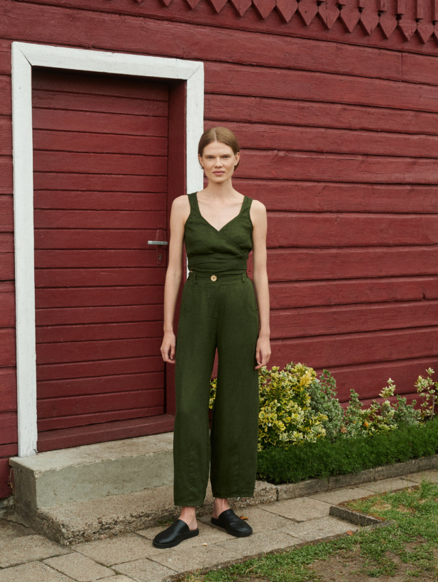 Model posing in summer clothing set of waffle linen trousers and wrap top in forest green near the red summer cottage