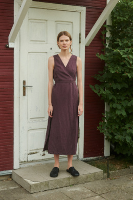 model wearing a V-neck linen wrap dress in eggplant violet with side slits and midi length while standing outside summer house