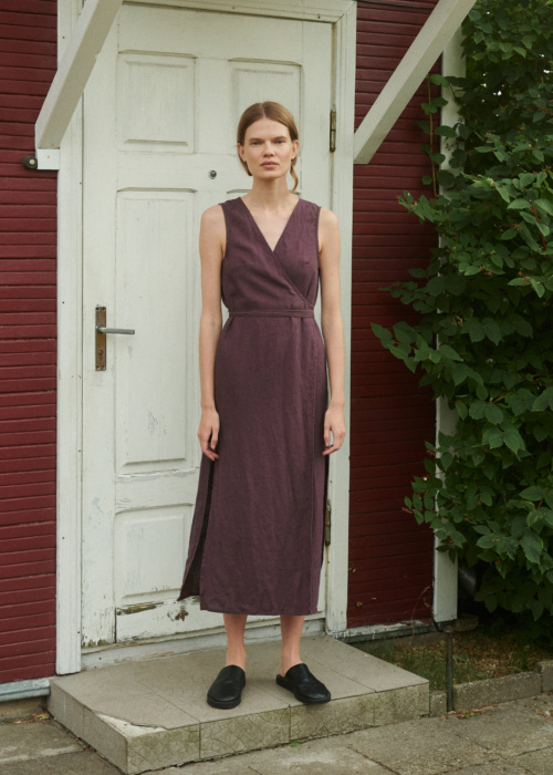 model wearing a V-neck linen wrap dress in eggplant violet with side slits and midi length while standing outside summer house