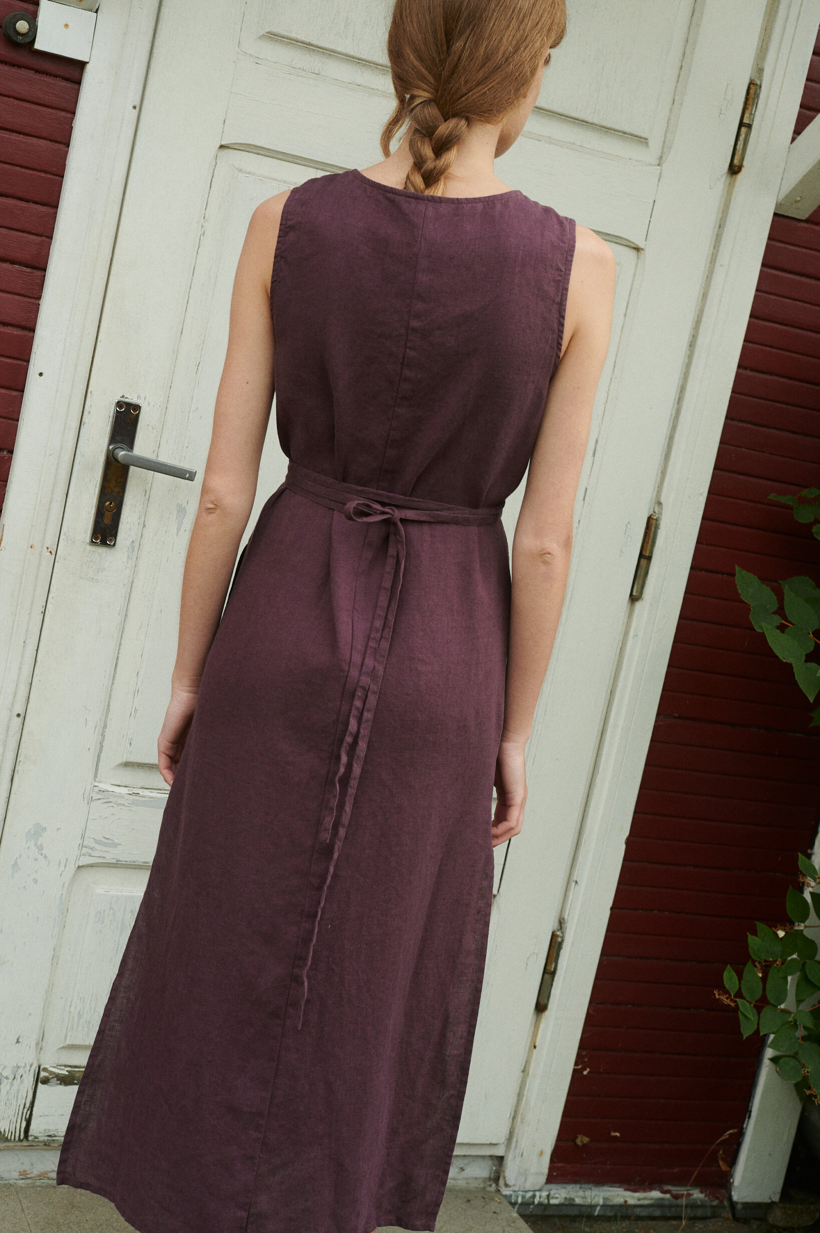 a back view of summer linen wrap dress in eggplant violet near the wide door