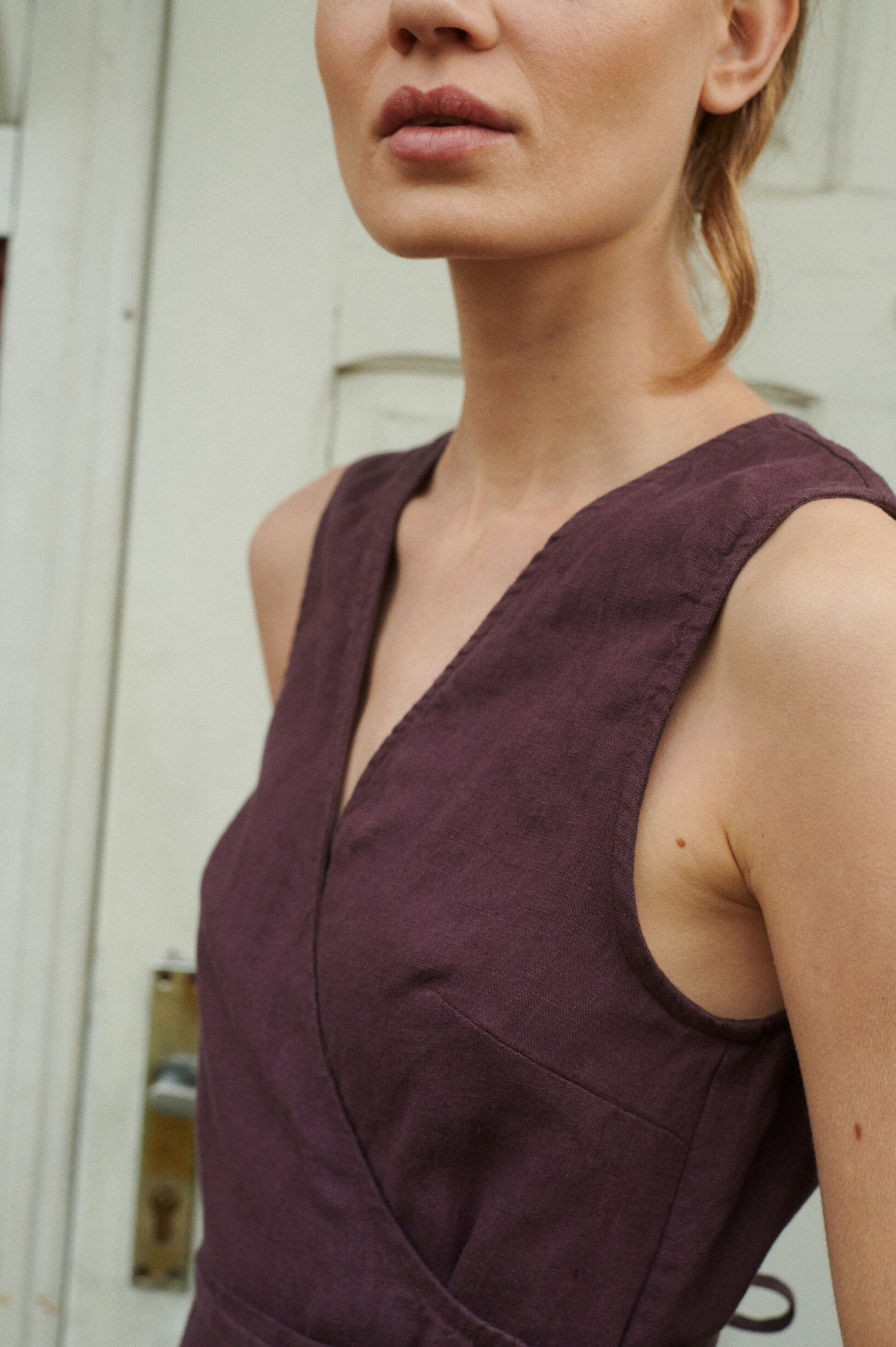 a close up of model wearing a natural summer linen V-neck wrap dress in eggplant violet