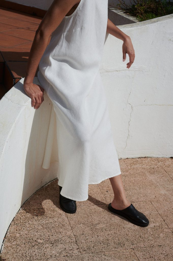 Detail shot of milky white linen fabric on Alba dress, showing natural texture and fluid drape falling in soft pleats.