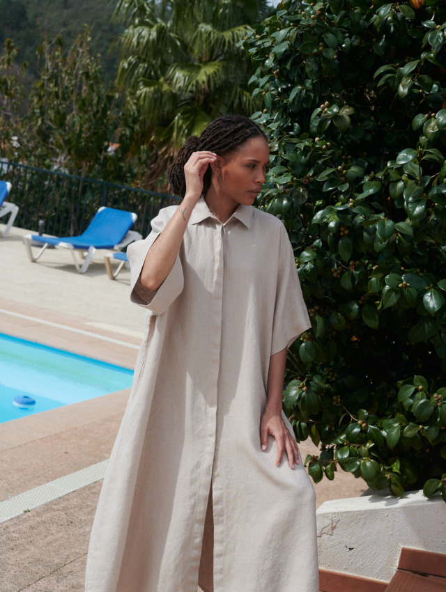 Woman posing in an extra oversized maxi beige linen dress with loose-fitting sleeves and a shirt collar