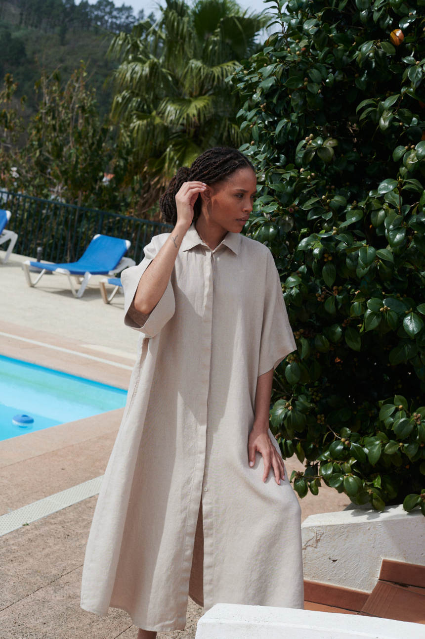 Woman posing in an extra oversized maxi beige linen dress with loose-fitting sleeves and a shirt collar