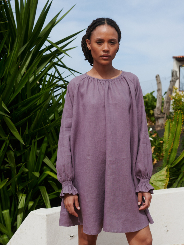 Model wearing a dusty lavender loose-fitting mini linen dress with a round neck and long sleeves