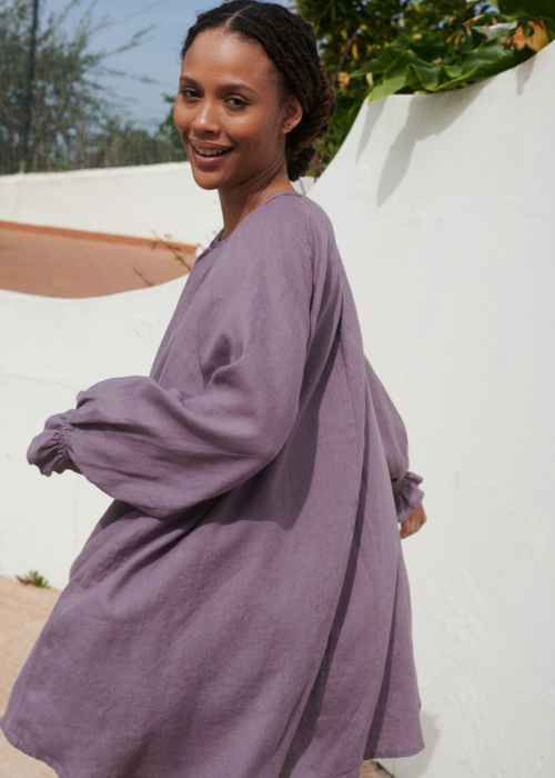 Model in a flowy oversized mini linen dress with long sleeves and elasticated cuffs