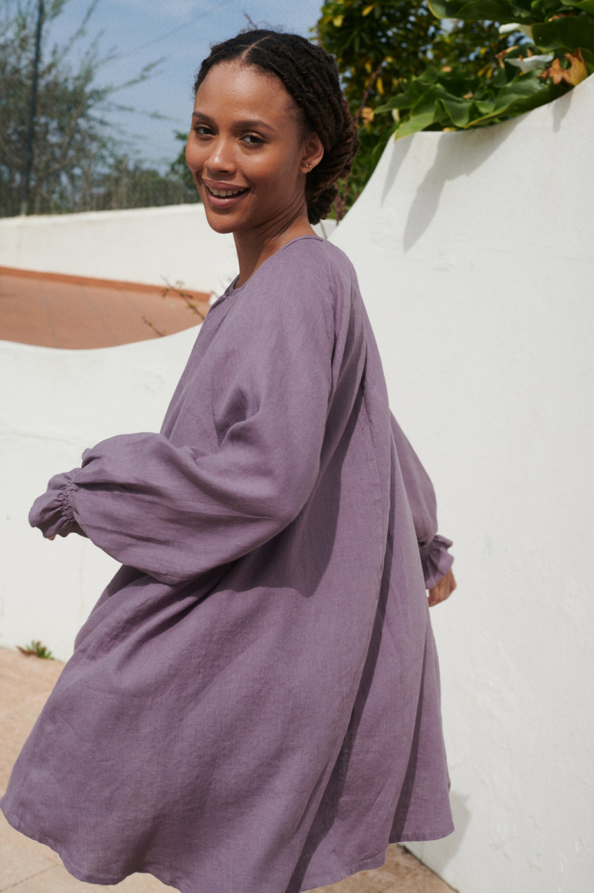 Model in a flowy oversized mini linen dress with long sleeves and elasticated cuffs