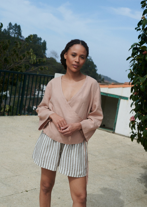 Model wearing lightweight cacao stripes linen shorts and an oversized long sleeve peach linen wrap top outfit