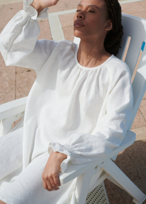 woman sitting in a milky white linen Agata dress with a mini-length hem, oversized fit, and full-length balloon sleeves