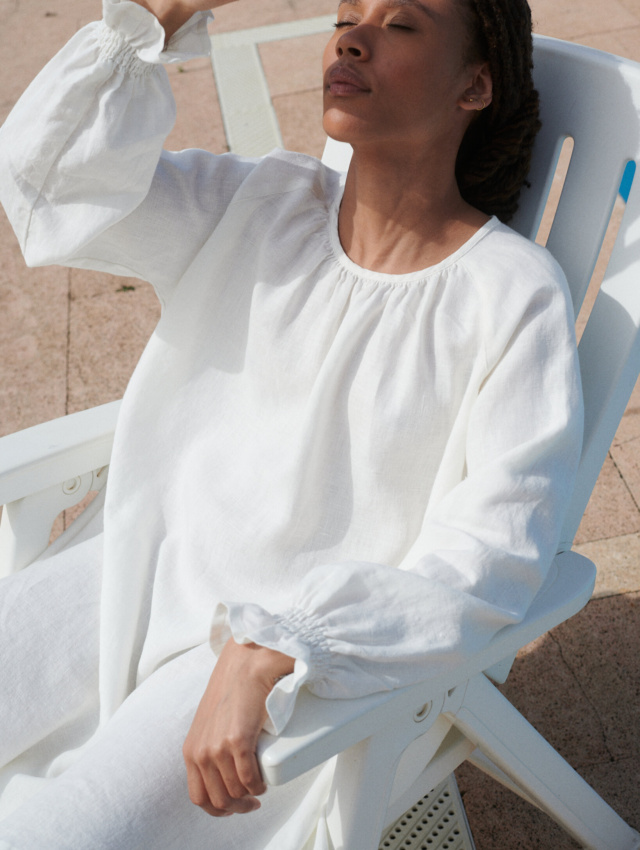 woman sitting in a milky white linen Agata dress with a mini-length hem, oversized fit, and full-length balloon sleeves