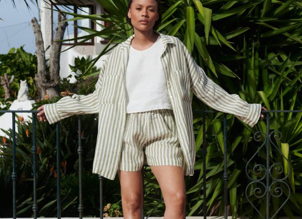 Model in casual oversized linen button down shirt with matching striped linen shorts combo paired with a white cropped linen top