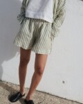 Woman wearing a cropped white linen top with a loose-fitting olive stripes linen shirt and matching shorts with pockets