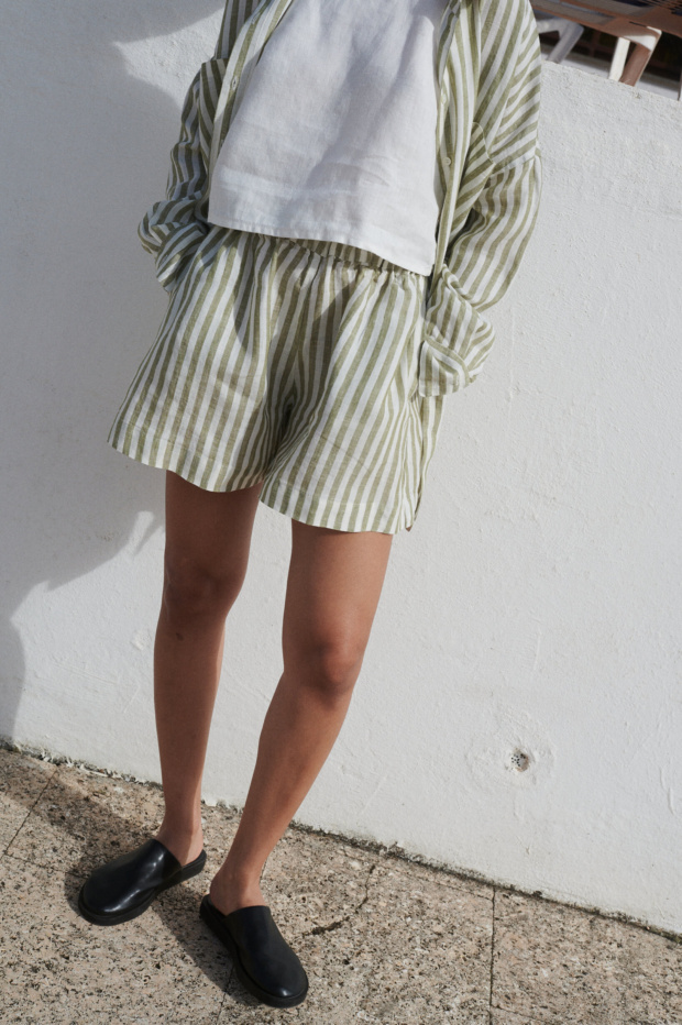 Woman wearing a cropped white linen top with a loose-fitting olive stripes linen shirt and matching shorts with pockets