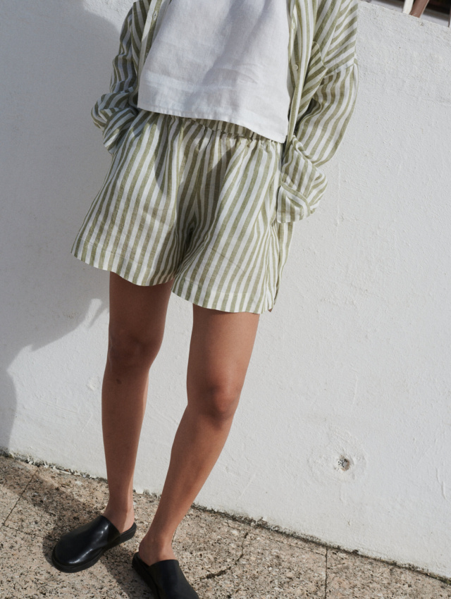 Woman wearing a cropped white linen top with a loose-fitting olive stripes linen shirt and matching shorts with pockets