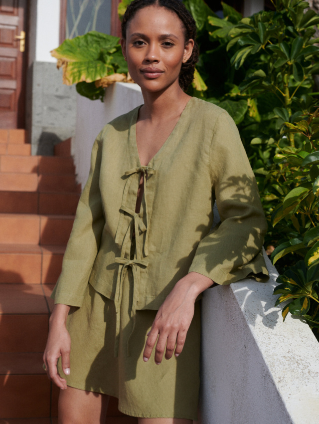 a woman wearing a linen set featuring a tie-up front top paired with a short skirt in olive linen fabric