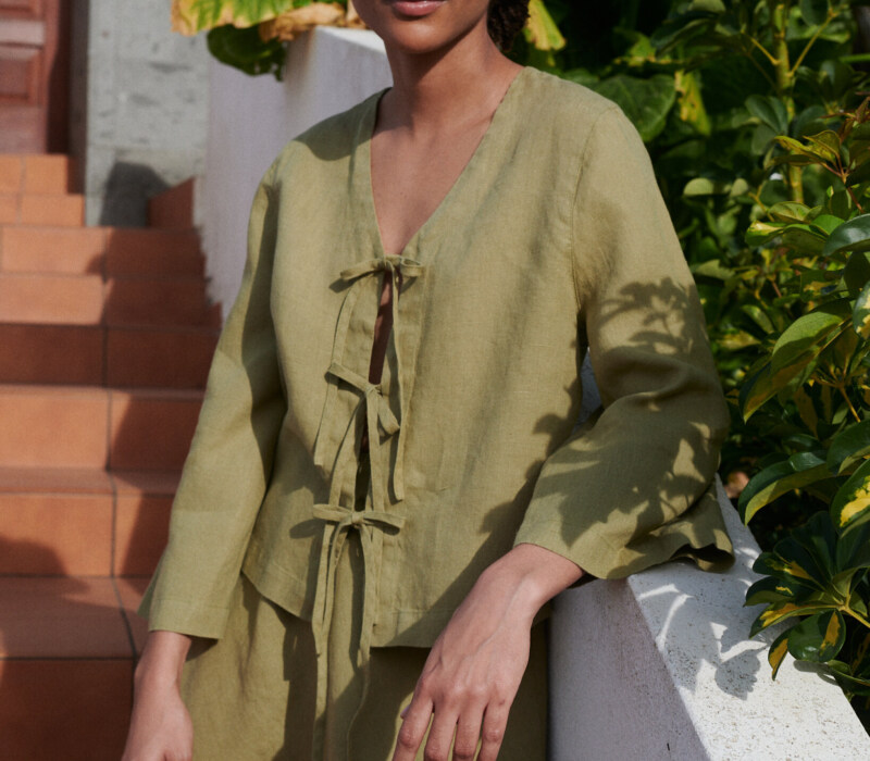 a woman wearing a linen set featuring a tie-up front top paired with a short skirt in olive linen fabric