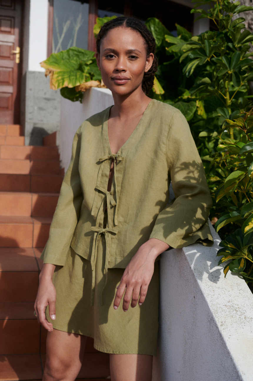 a woman wearing a linen set featuring a tie-up front top paired with a short skirt in olive linen fabric