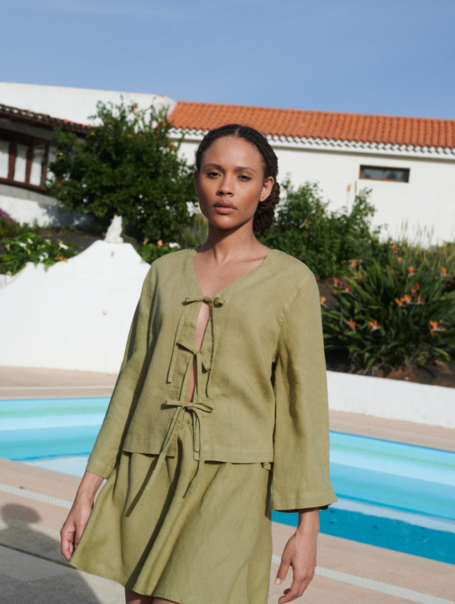 A woman draped in a tie-up front top and a short skirt in olive linen fabric,