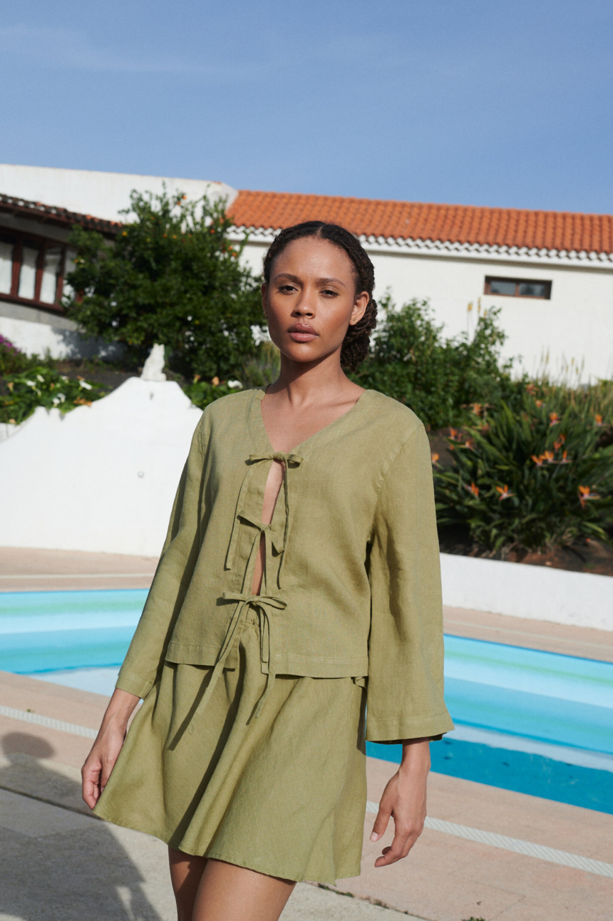 A woman draped in a tie-up front top and a short skirt in olive linen fabric,