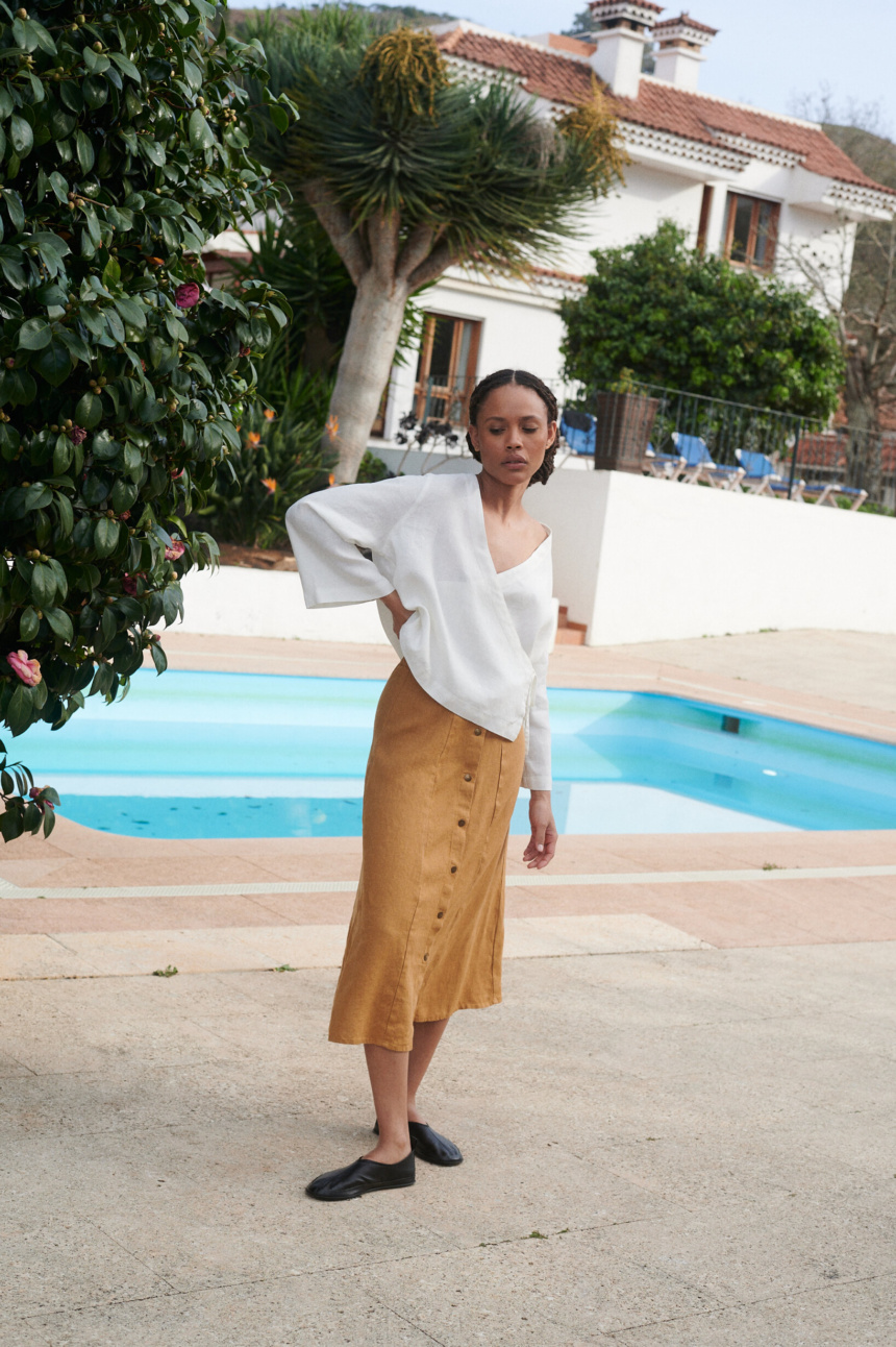 Model wearing a loose-fitting white linen wrap top and a camel color midi linen skirt with snap buttons in the front