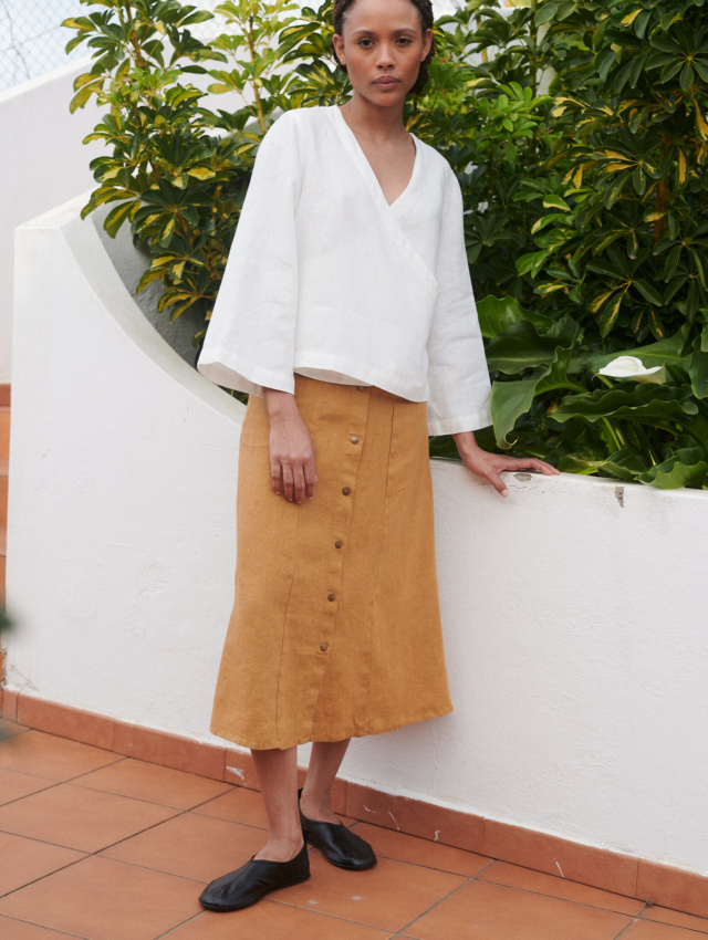 Model wearing a loose-fitting white linen V-neck wrap top and a camel color midi linen skirt with metal snap buttons