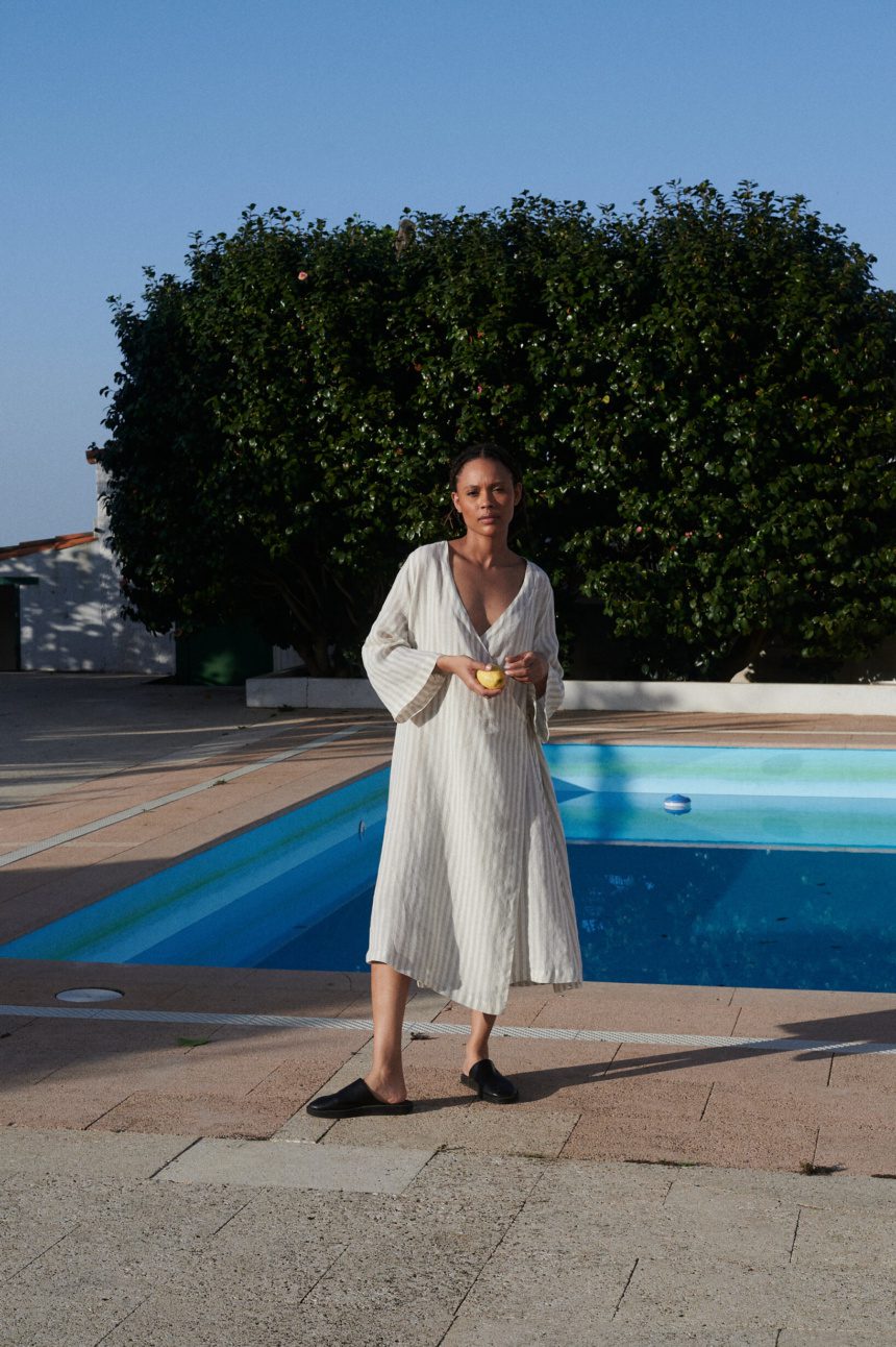 A woman exudes grace in a wrap dress crafted from light linen fabric, featuring natural grey stripes and an oversized silhouette