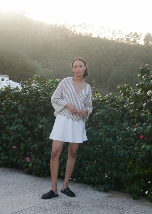 a woman wearing a wrap top in light linen stripes paired with a milky white linen short skirt