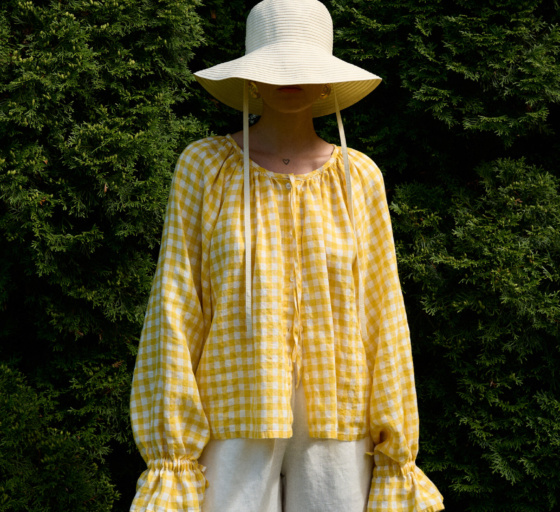 model wearing gingham linen summer top in yellow and white checks with a hat