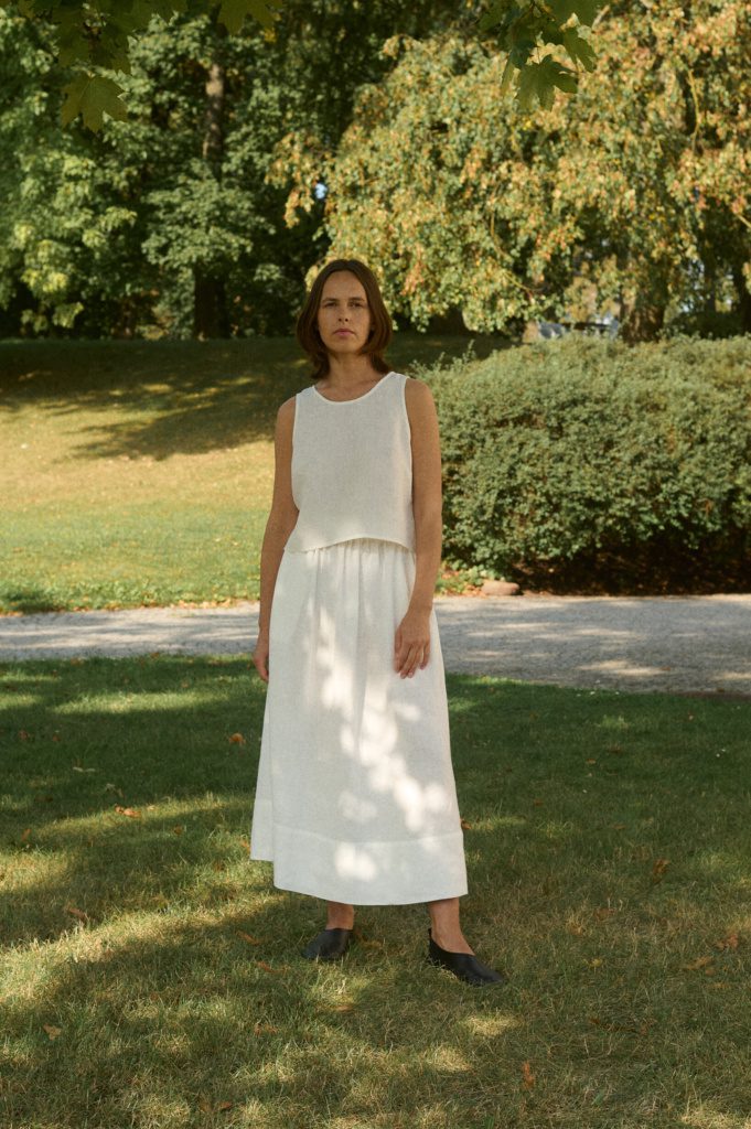 A woman wearing the Sadie sleeveless linen top, a staple piece in any linen minimalist wardrobe, paired with light skirt