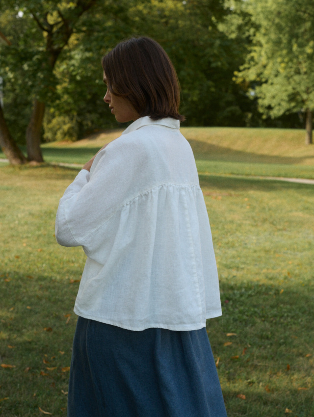 Woman wearing a flowy linen white top with ruffled back detail and a blue linen wool blend skirt