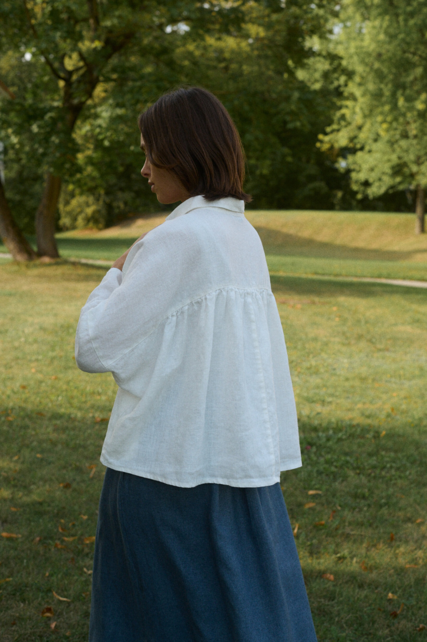 Woman wearing a flowy linen white top with ruffled back detail and a blue linen wool blend skirt