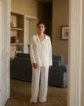 Model wearing a relaxed nightwear set in lightweight milky white linen, featuring a long-sleeve button-up shirt and wide-leg pants